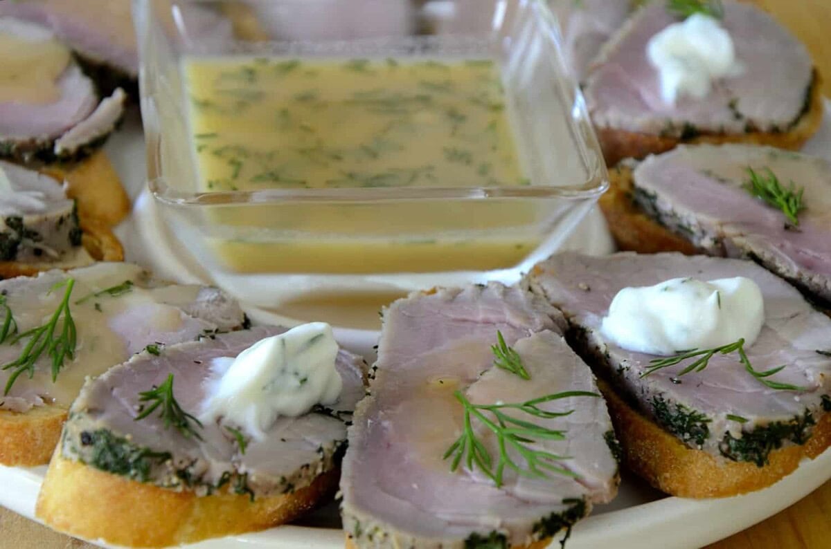Platter of crostini topped with slice of dill cured pork tenderloin and a sweet mustard sauce