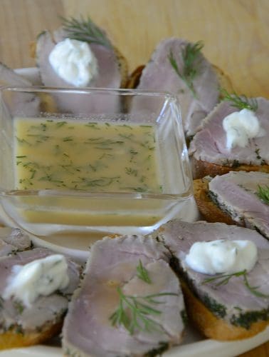 Platter of crostini topped with slice of dill cured pork tenderloin and a sweet mustard sauce