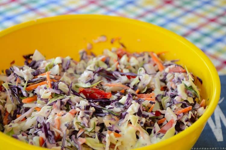 Bright yellow bowl filled with coleslaw made from red and green cabbage with red pepper