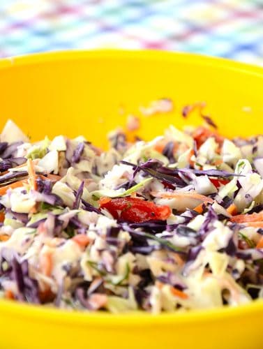 Bright yellow bowl filled with coleslaw made from red and green cabbage with red pepper