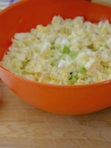 Bowl of egg potato salad with potatoes, eggs and green onion beside,