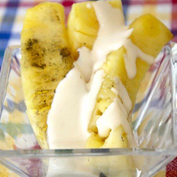 Spears of grilled pineapple in a dish with Tequila cream drizzled over