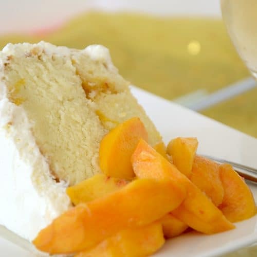 Slice of Peach and Prosecco cake with whipped cream frosting and fresh peach slices on the side