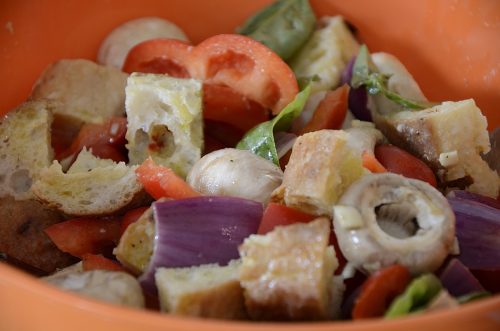 Sausage, pepper, onion and mushroom pieces marinating in dressing in a large bowl.