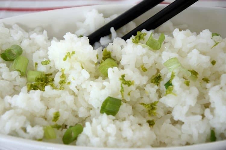 Bowl of fluffy jasmine rice with grated lime rind and green onion garnish in a bowl with chop sticks
