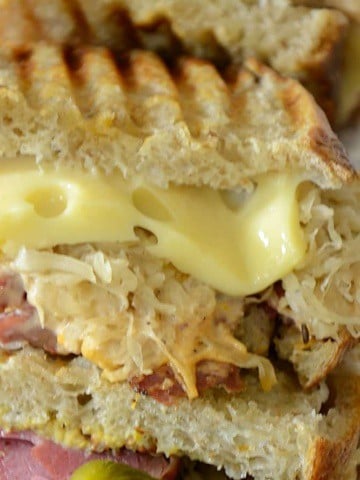 Two halves of a Reuben Sandwich on a board with Swiss Cheese and Sauerkraut oozing out of the sandwich