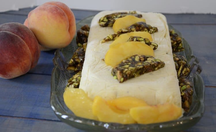 Semifreddo on a plate garnished with fresh peaches and pistachio brittle.