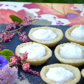 Maple tarts with whipped cream topping on a tray on an autumn table cloth.