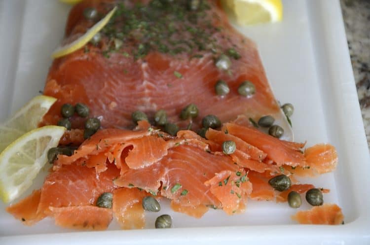 Fillet of Gin cured trout thinly sliced with capers and lemon on a cutting board.