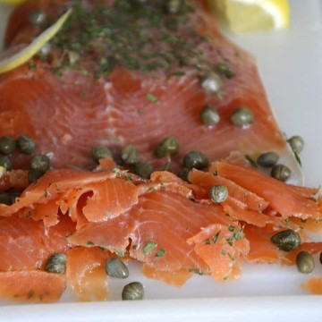 Fillet of Gin cured trout thinly sliced with capers and lemon on a cutting board.