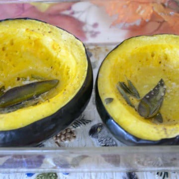 Two roasted acorn squash halves with butter and sage.
