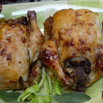 Two stuffed Cornish hens on a platter with celery leaves and sage garnish.