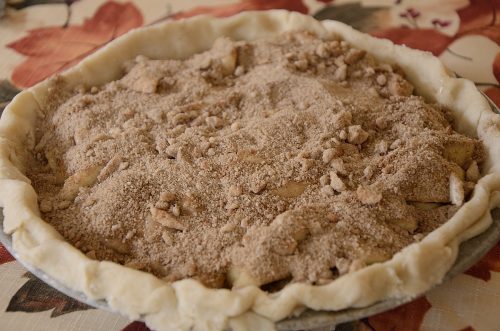 Pie shell with apple wedges and cream topping and streusel crumbs on top.