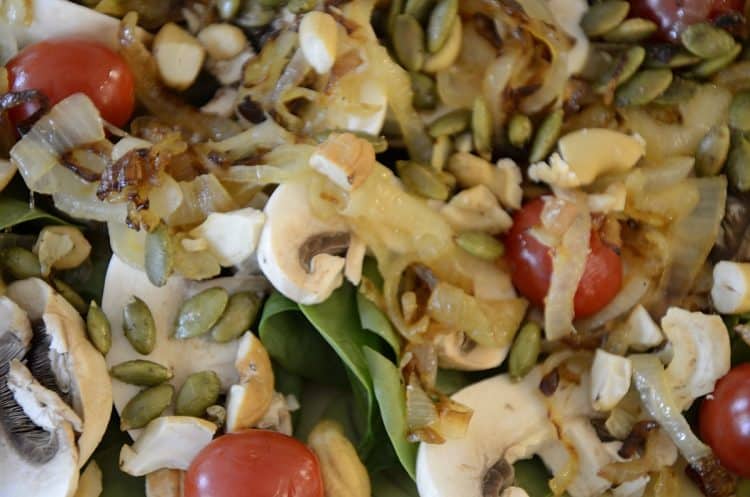Salad on platter covered in cashews, pumpkin seeds, caramelized onions, grape tomatoes and sliced mushrooms.