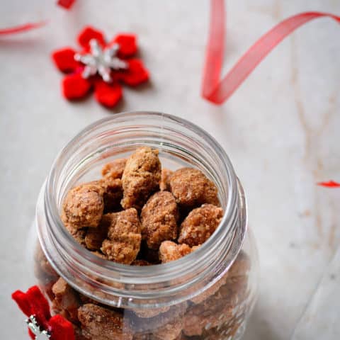 Jar of spicy coated almonds with christmas ribbon and decoration beside.