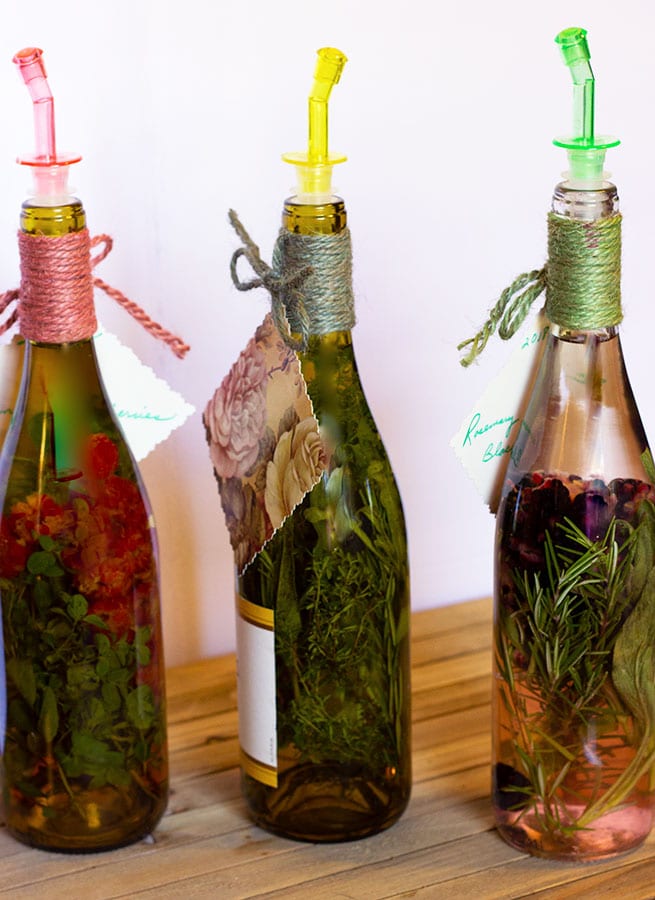 Three wine bottles filled with herbs and fruit with colourful stoppers.