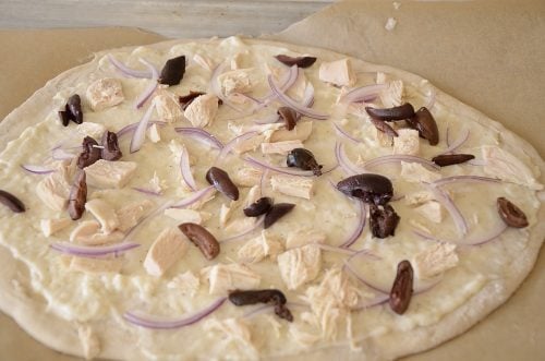 Uncooked thin crust pizza with garlic white sauce, chicken, red onion and black olives.