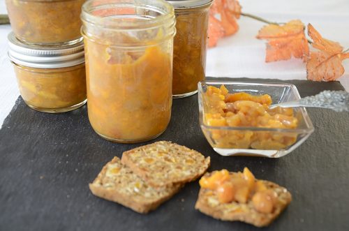 Persimmon chutney on an Artisanal cracker with jars of chutney in the background.