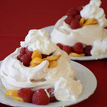 Two pavlovas on dessert plates topped with fresh persimmon slices, raspberries and whipped cream.