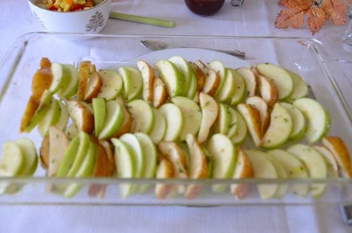 Slices of apples and pears in a baking pan tossed in olive oil and minced rosemary.