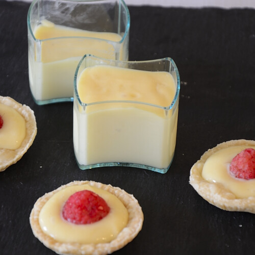 Tarts shells filled with lemon custard and topped with a fresh raspberry. Small serving cups of lemon custard on the side.