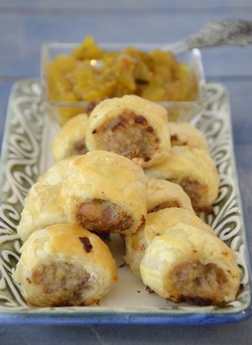 Australian sausage roll baked golden brown puff pastry, cut into pieces on a plate with mustard relish for garnish.