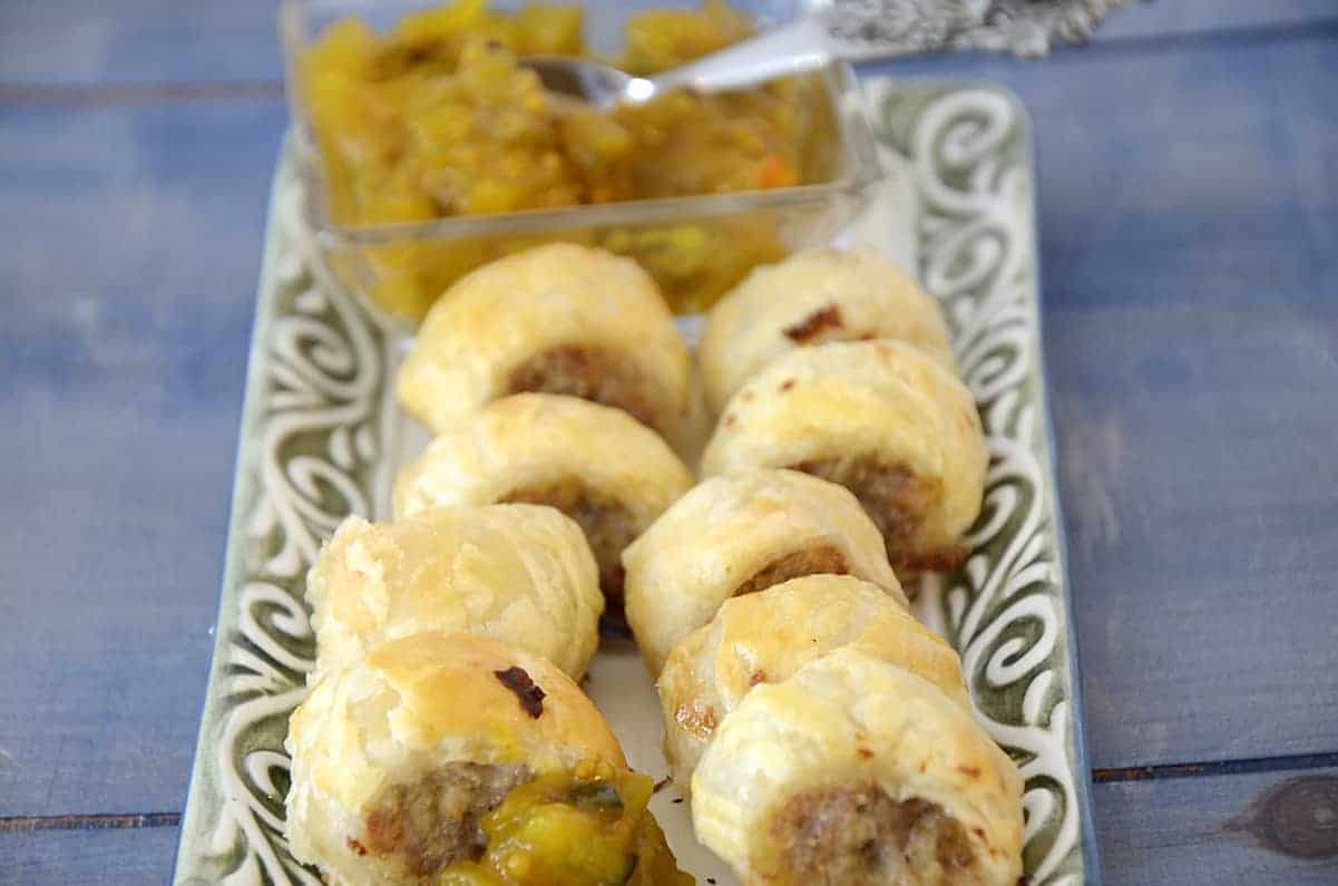 Australian sausage roll baked golden brown puff pastry, cut into pieces on a plate with mustard relish for garnish.