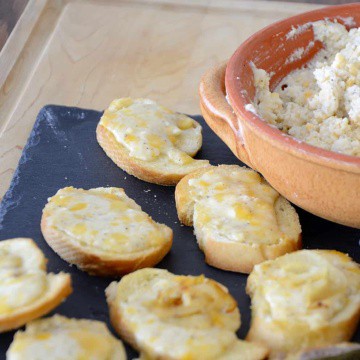 Pot of fromage fort with toasted baguette slices topped with melted fromage fort.