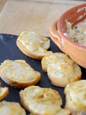 Pot of fromage fort with toasted baguette slices topped with melted fromage fort.