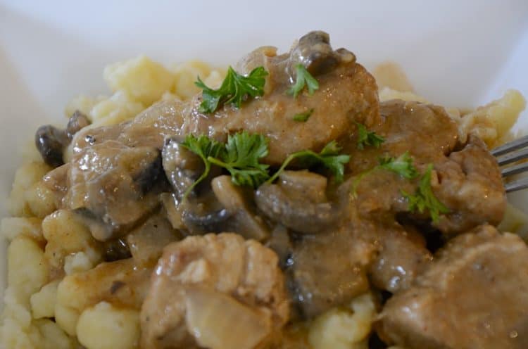 Close up of juicy, creamy cubes of cooked pork and mushrooms over German Spatzle noodles.