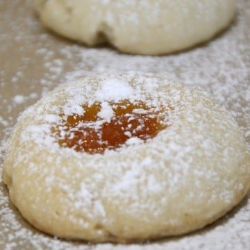 Thumbprint cookies with apricot jam filling on baking sheet.