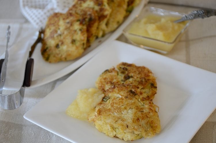 Fried sauerkraut cakes on a plate with a dollop of applesauce.