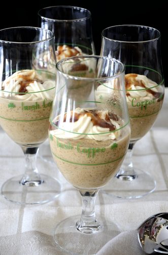 Four Irish Coffee glasses filled with Irish Coffee mousse and topped with whipped cream and caramel sauce.