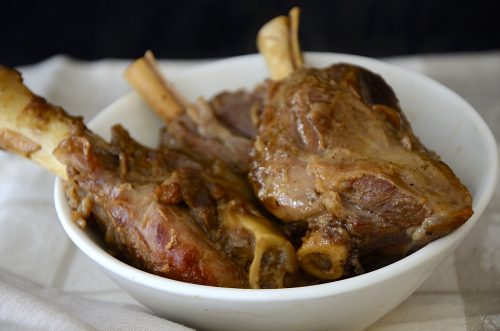 Three roasted lamb shanks in a bowl.