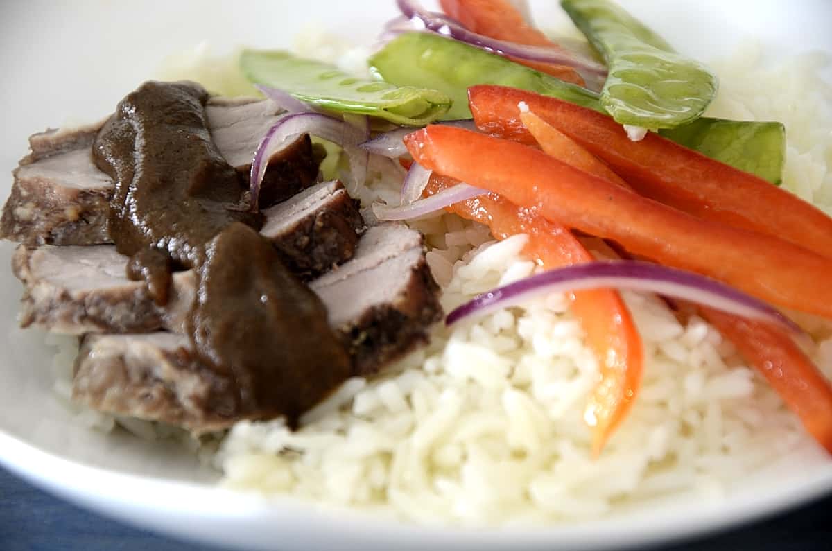 Pork tenderloin slices with spicy prune sauce on a bed or rice with snow peas and red peppers on the side.
