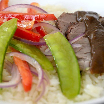Pork tenderloin slices with spicy prune sauce on a bed or rice with snow peas and red peppers on the side.