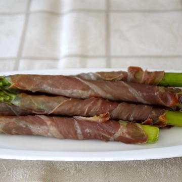 Spears of asparagus wrapped in prosciutto in a dish fresh from the air fryer.