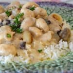 Close up of French rabbit in mustard sauce with pearl onions and mushrooms on a bed of rice.