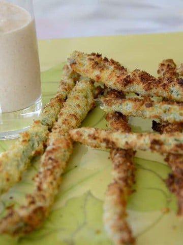 Breaded asparagus spears on a tray with dipping sauce.