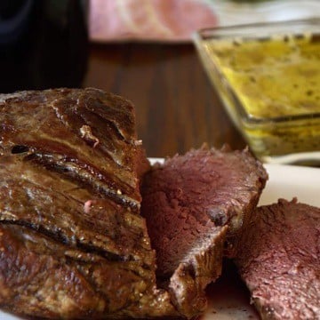 Medium rare beef tenderloin on a platter with Cafe de Paris sauce on the side.
