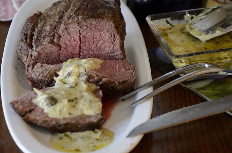Medium rare beef tenderloin sliced on a platter with Cafe de Paris sauce.