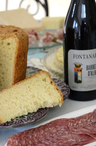 Tall loaf of Italian Easter bread with a wedge cut out of it with a bottle of red wine beside.