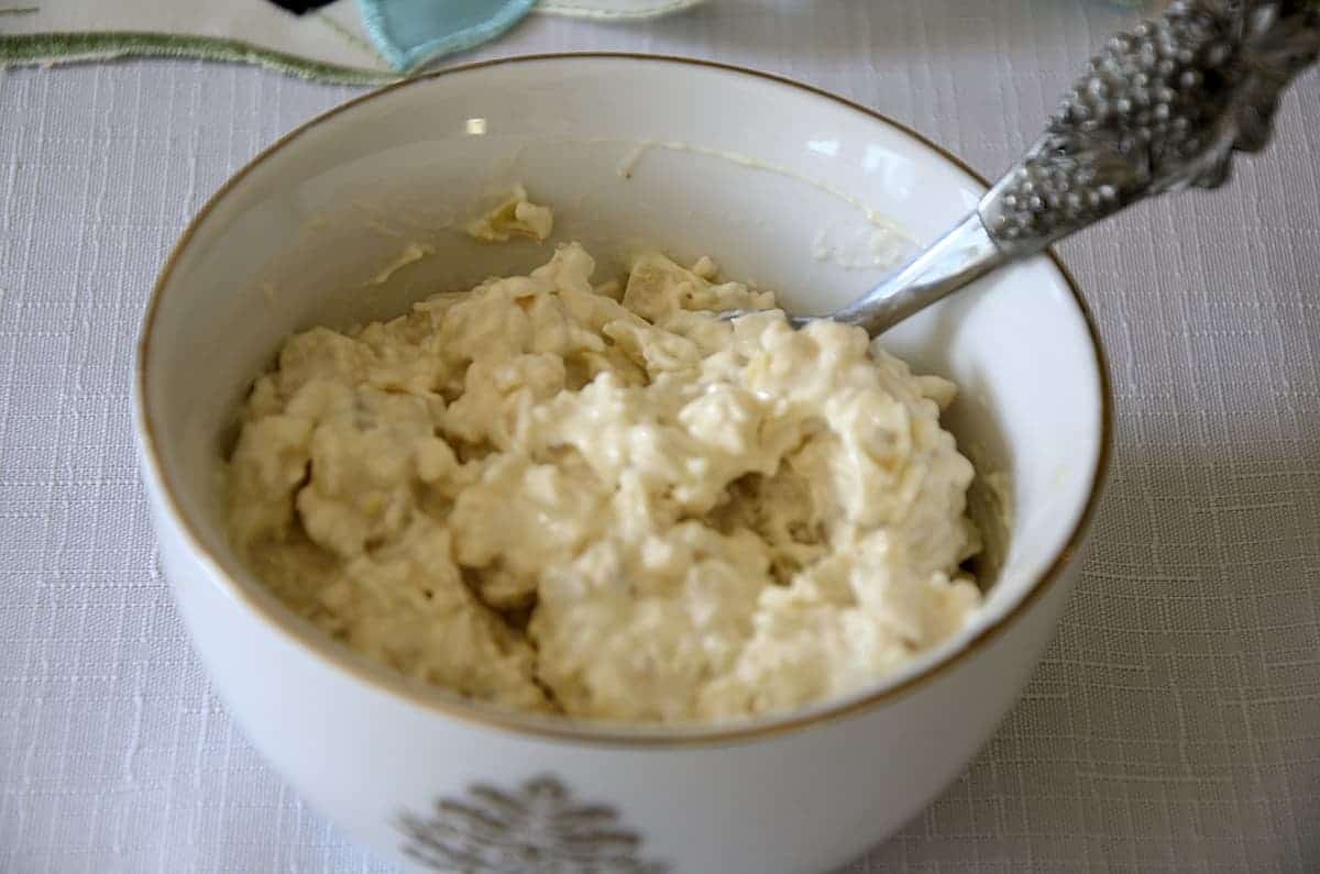 Creamy, garlicky artichoke dip in a bowl with small serving spoon.