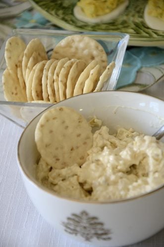 Creamy artichoke dip being spread on a rice cracker.