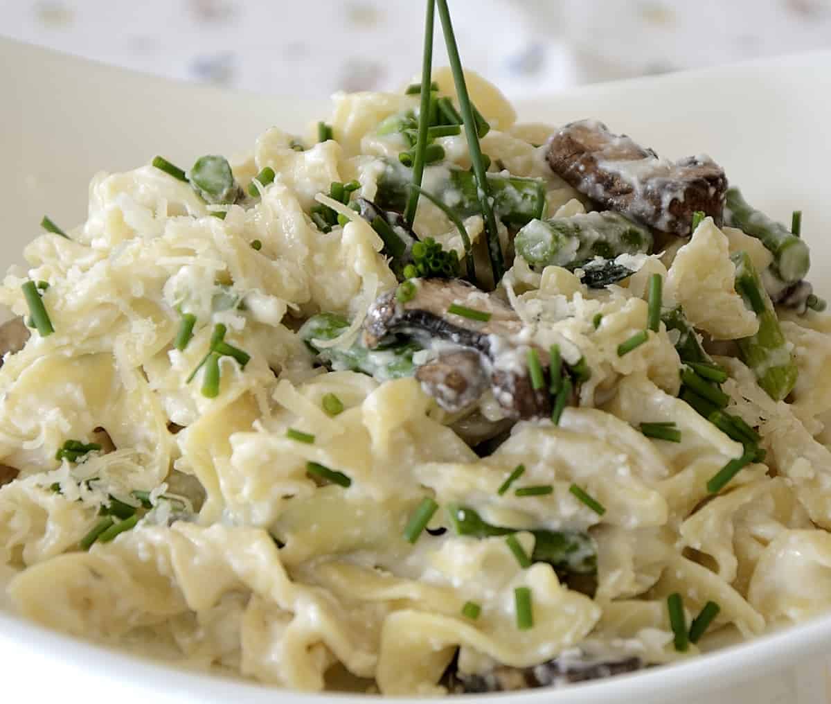 Egg noodles with creamy ricotta, lemon sauce, asparagus, mushrooms and garnished with chives.