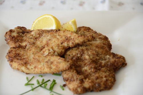 Crispy air fried chicken cutlets with a slice of lemon on a plate.