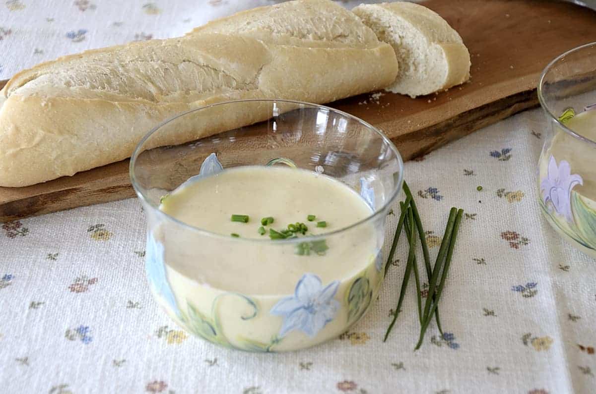 Potato leek soup garnished with fresh chives beside a baguette of fresh bread.