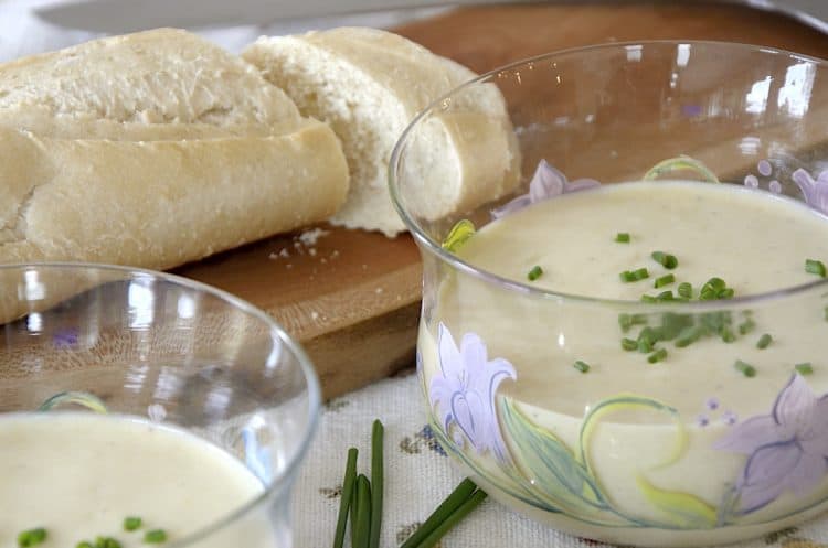 Potato leek soup garnished with fresh chives beside a baguette of fresh bread.