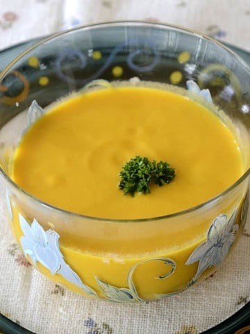 Bowl of bright yellow carrot soup with parsley garnish.