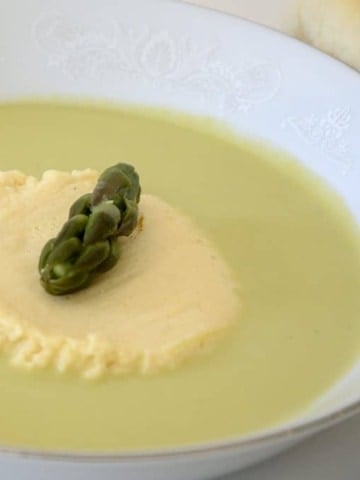 Creamy asparagus soup in a white shallow soup bowl with a Parmesan custard island in the center.